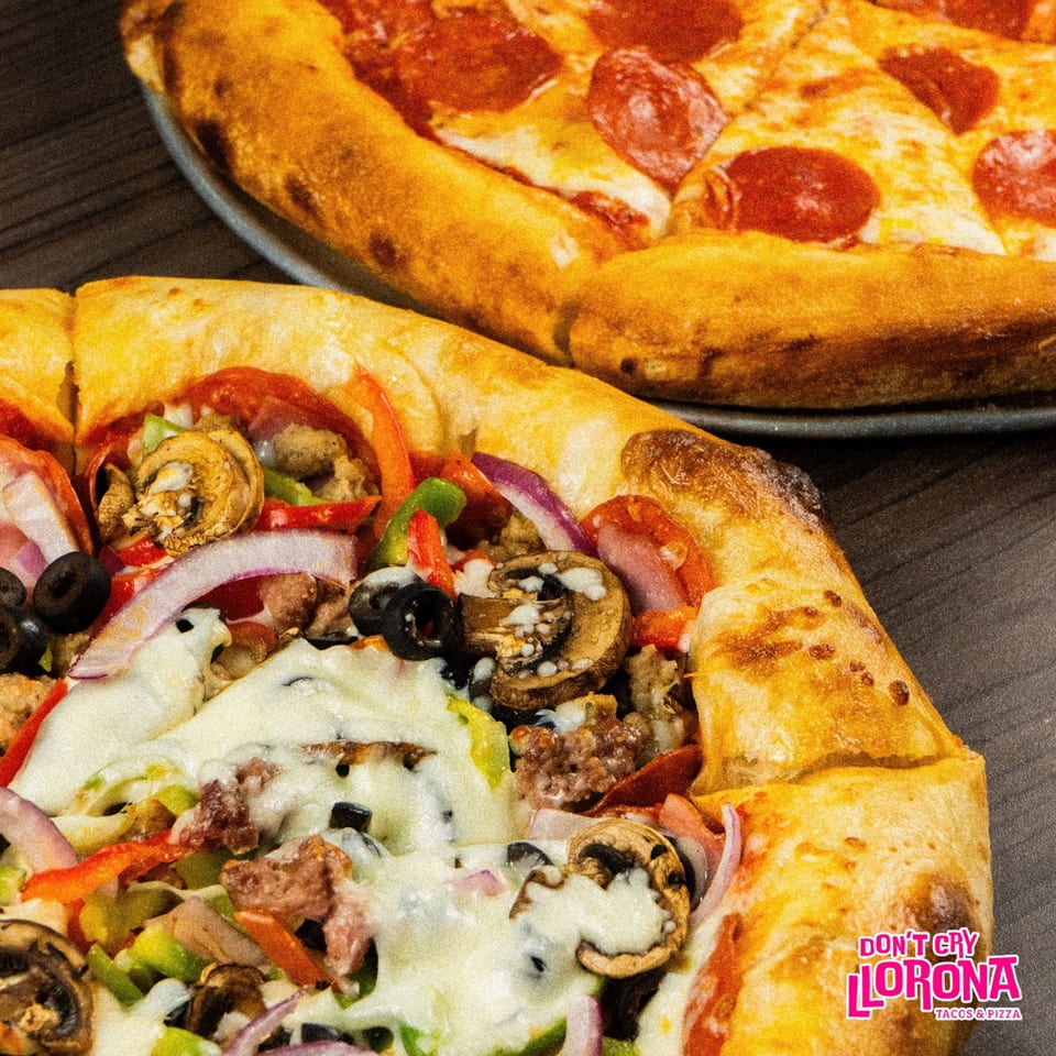 Two pizzas, one pepperoni and one with various toppings, on a dark wooden surface.